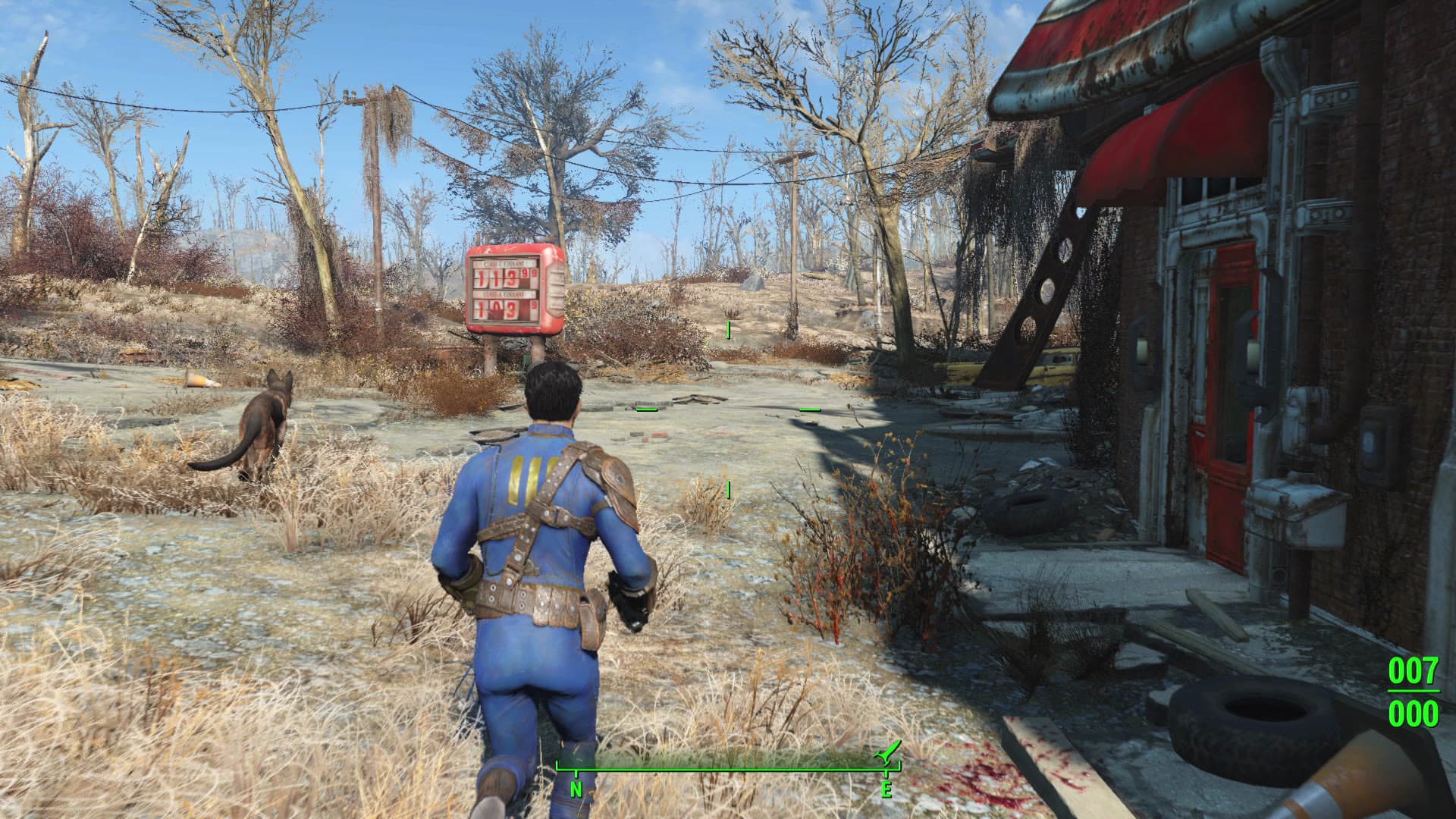 The Sole Survivor travels with Dogmeat beside a ruined service station, with Fallout 4’s compass and ammunition HUD visible.